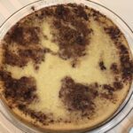 A fully baked milk tart in a glass dish with a golden-brown cinnamon-dusted crust, resting on a striped tablecloth.