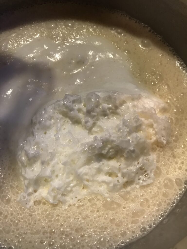 A close-up shot of frothy, white beaten egg whites being folded into a bubbly milk and flour tart batter in a mixing bowl.