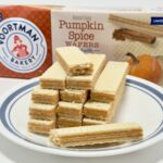 A symmetrical stack of Voortman Pumpkin Spice Wafers on a blue-rimmed white plate, with the product packaging and a decorative pumpkin in the background.
