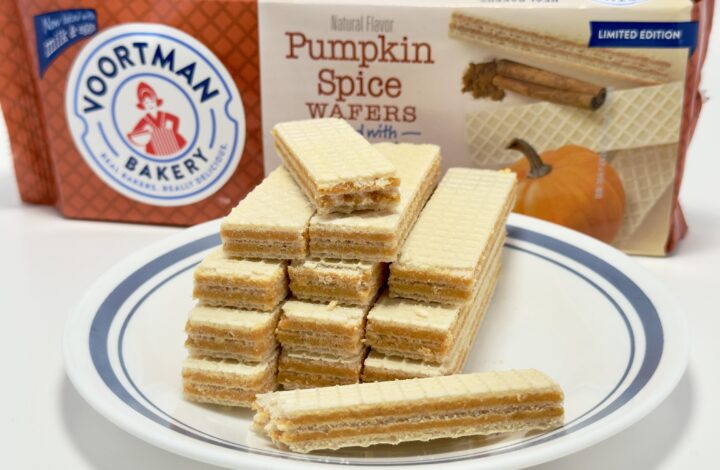 A symmetrical stack of Voortman Pumpkin Spice Wafers on a blue-rimmed white plate, with the product packaging and a decorative pumpkin in the background.