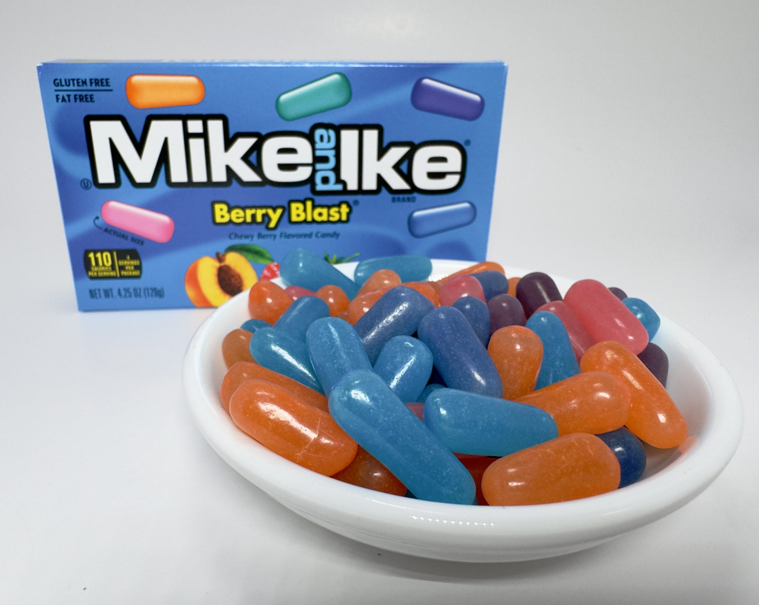 A white bowl filled with assorted Mike and Ike Berry Blast candies in front of the blue theater-sized box.