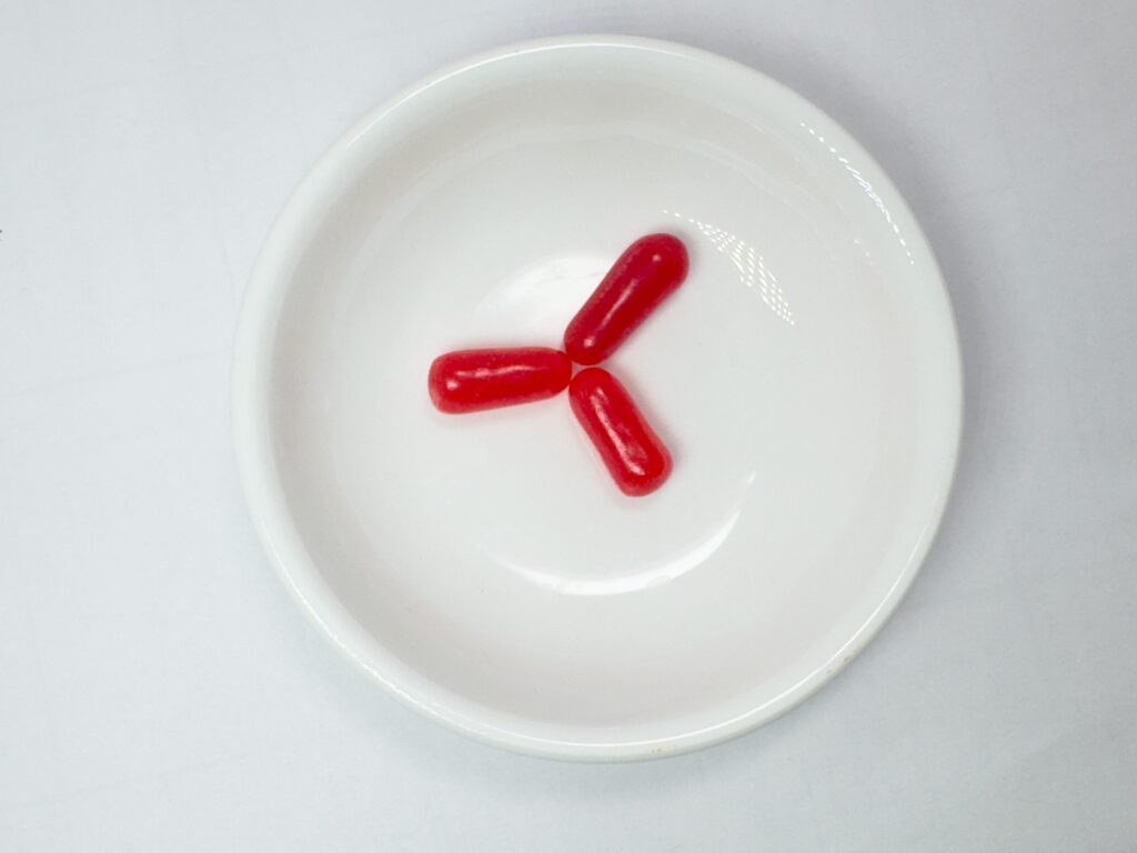 Three deep red Cherry flavored Mike and Ike candies in a white bowl.