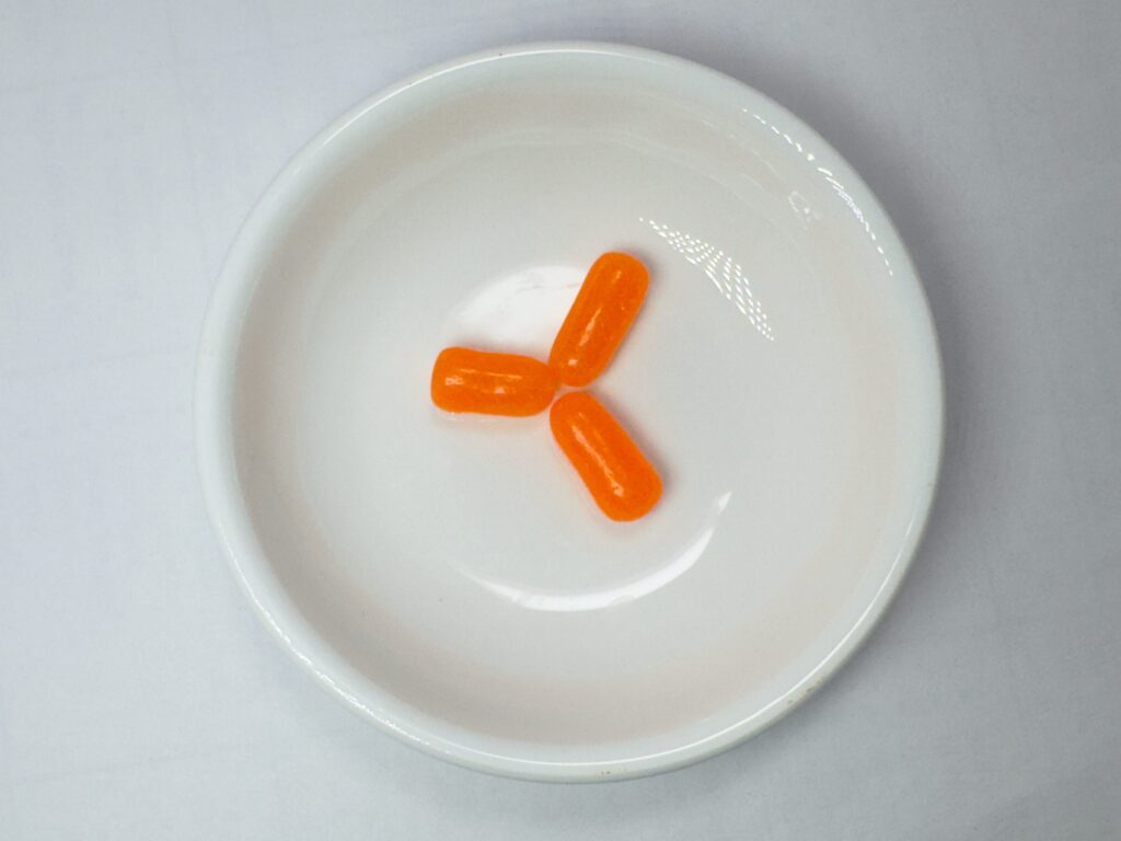 Mike and Ike Candy three orange flavored pieces on a white dish, showing the orange color of the candy.