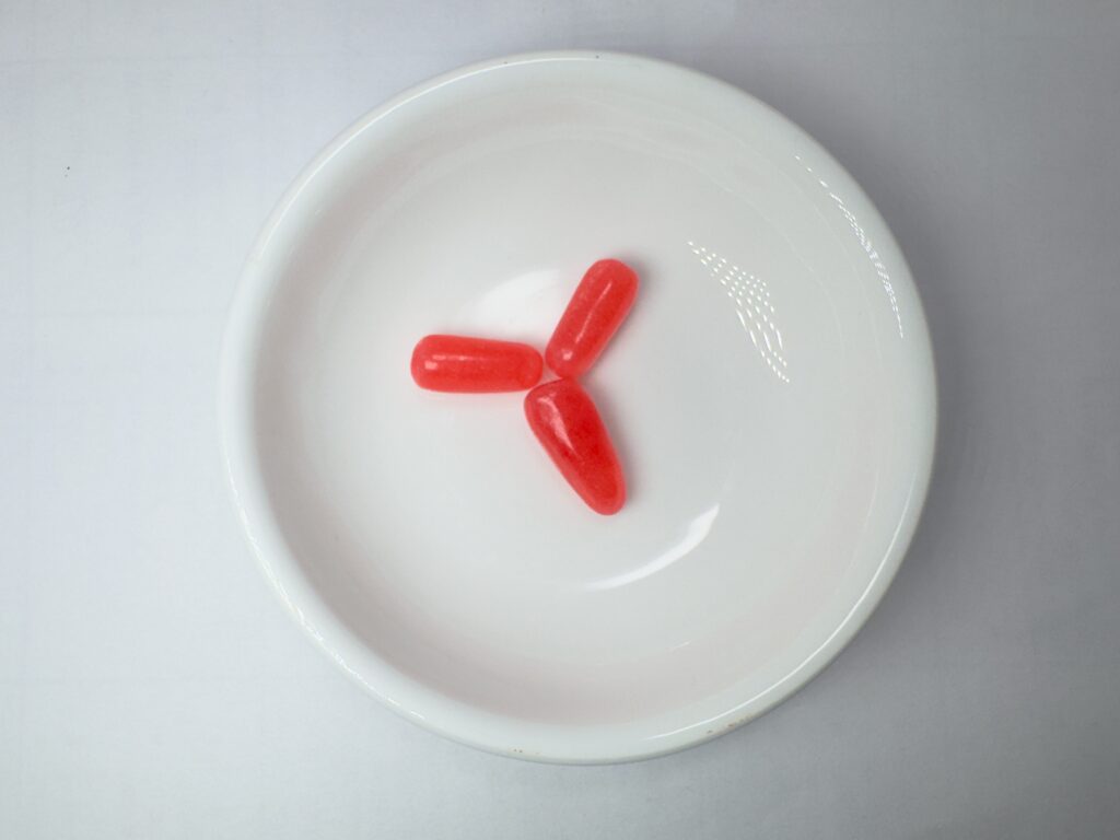Three pink Mike and Ike Strawberry flavored candies arranged in a white bowl.