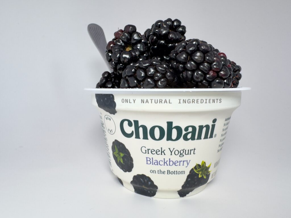 A close-up of a single cup of Chobani Greek Yogurt topped with fresh berries and silver spoon.