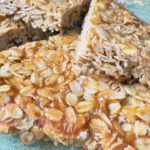 A high-detail, close-up shot of a golden-brown British oatmeal flapjack showing the glossy texture of Lyle’s Golden Syrup and old-fashioned rolled oats.