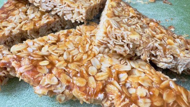 A high-detail, close-up shot of a golden-brown British oatmeal flapjack showing the glossy texture of Lyle’s Golden Syrup and old-fashioned rolled oats.