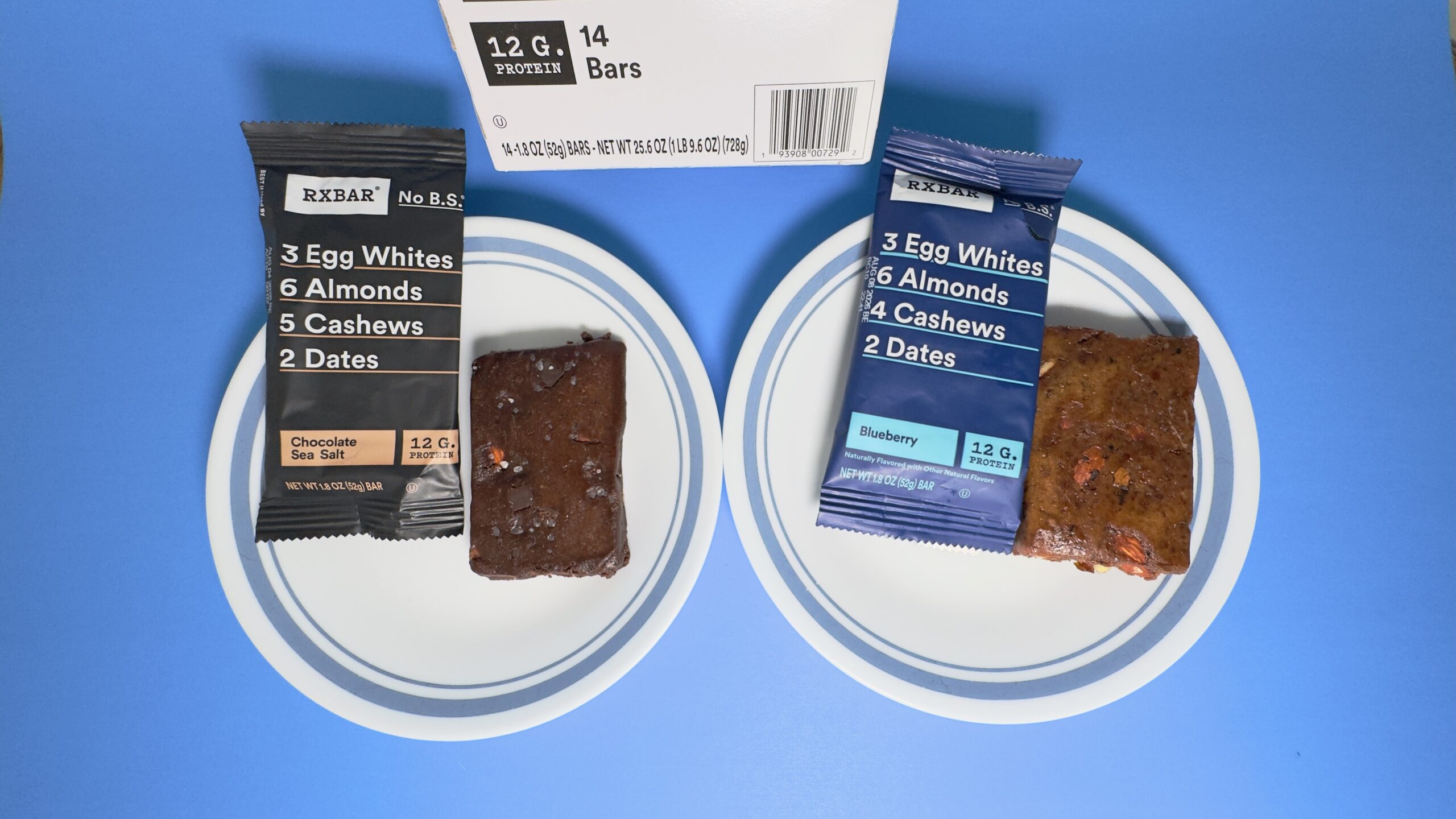 A 14-count variety pack of RXBARs from Costco featuring Chocolate Sea Salt and Blueberry flavors, with two unwrapped bars displayed on white plates.